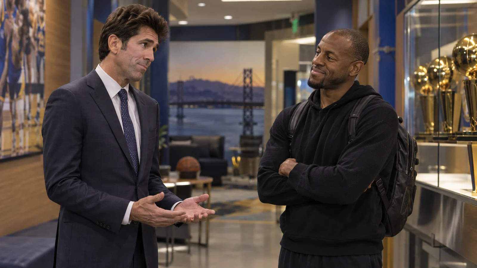 Satirical Warriors facility scene with a Bob Myers-like executive speaking apologetically to an Andre Iguodala-like former player beside championship trophies.