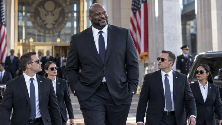 Satirical editorial image of a towering former basketball star in a dark suit arriving at a federal building with security agents.