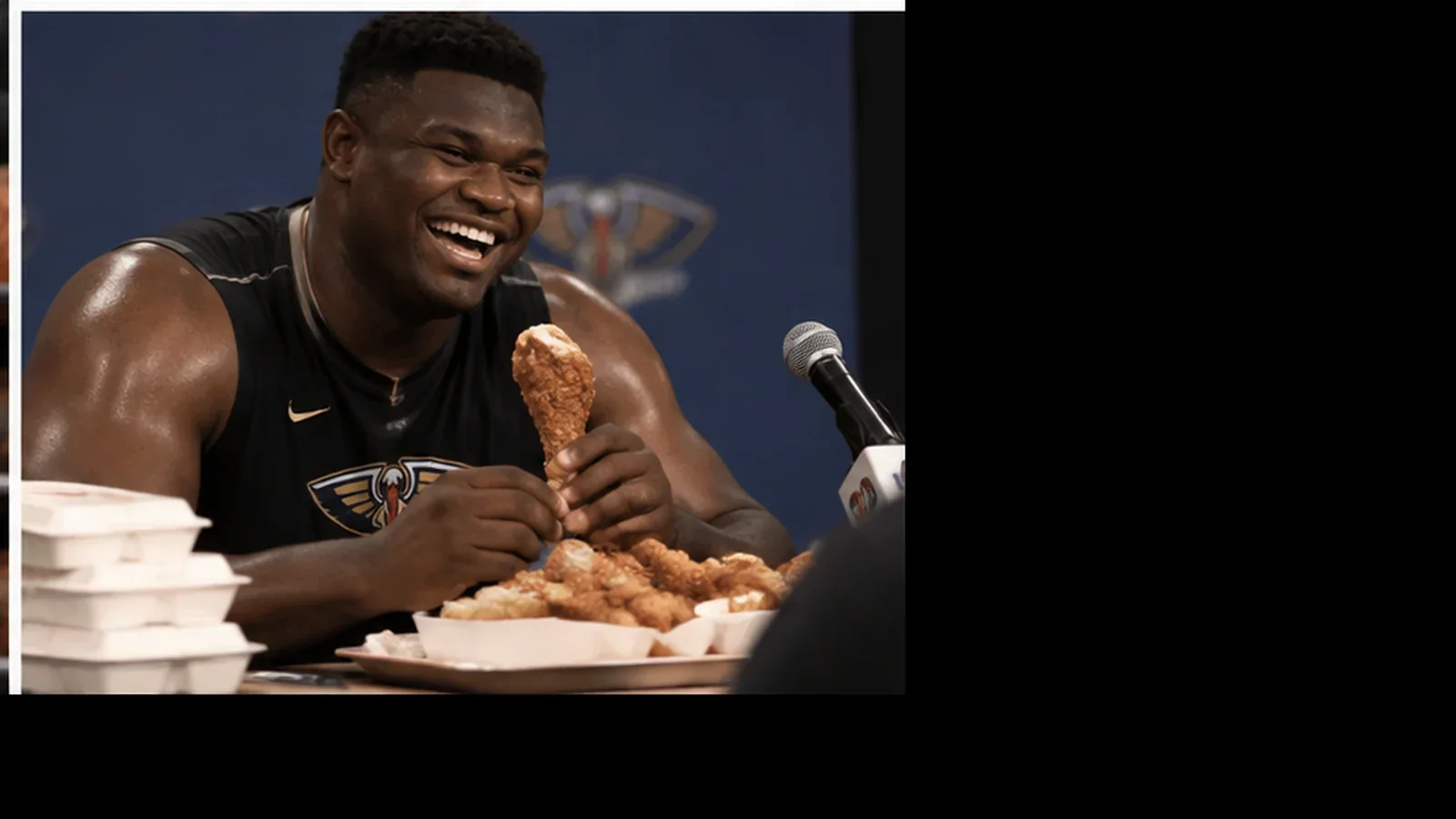 Satirical media-day press conference image of a smiling New Orleans basketball player seated at a table while eating fried chicken.